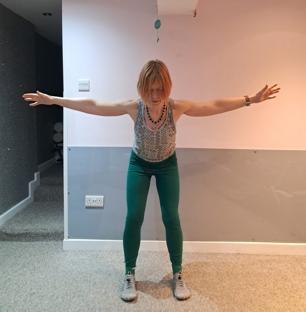 Author doing a hip hinge with arms doing a reverse flye exercise